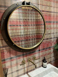 a bathroom with a round mirror and a plaid wallpaper